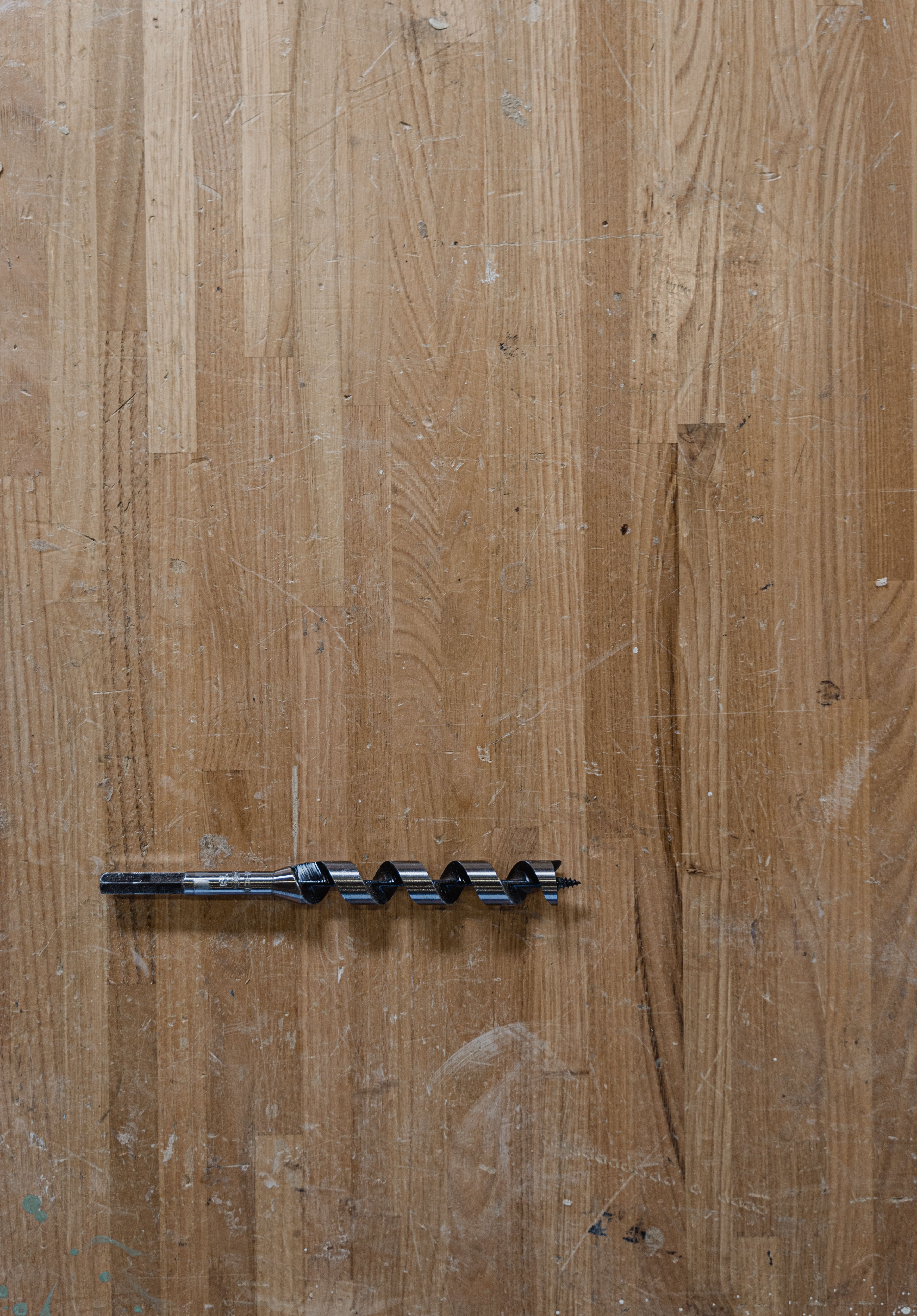 Close-up of a metal drill bit on a wooden surface, ideal for carpentry projects.