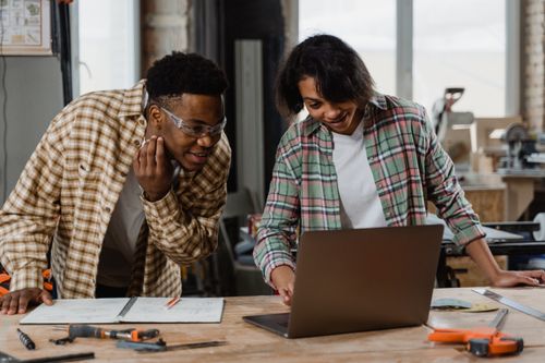 Free Two diverse adults collaborating in workshop, using laptop and planning design. Stock Photo
