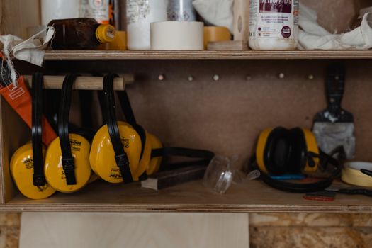 Yellow earmuffs and tools arranged on a shelf in a workshop setting.