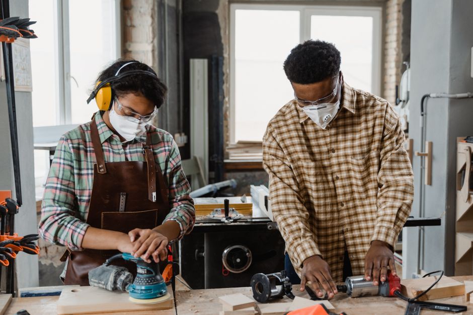 保護具を着用した2人の職人が作業場で道具を使って働いています。