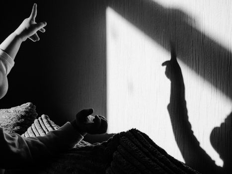 Black and white photo of a child creating hand shadows on a wall, evoking imagination and playfulness.