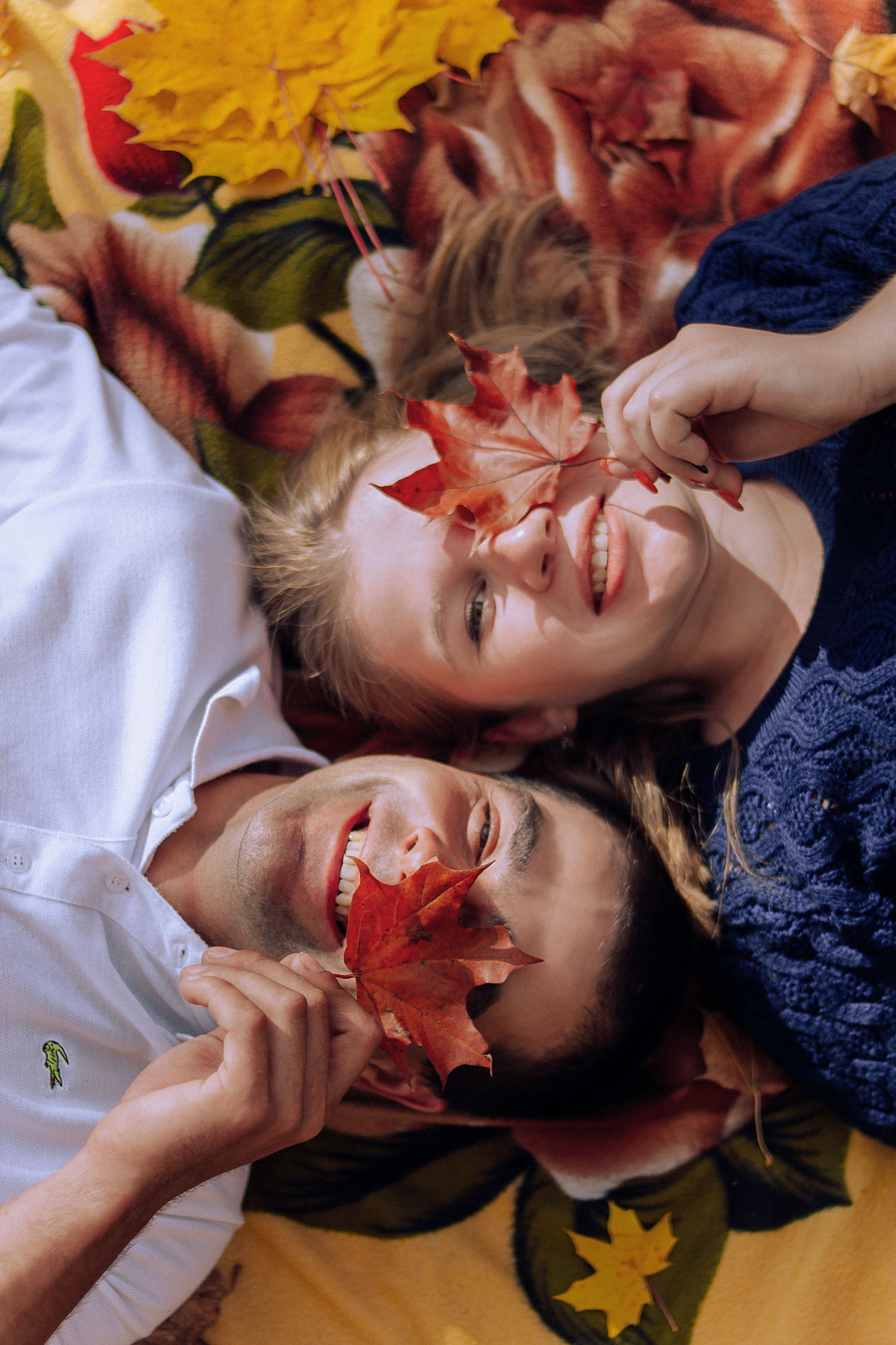 Smiling couple lying on a blanket with autumn leaves, showcasing joy and connection.