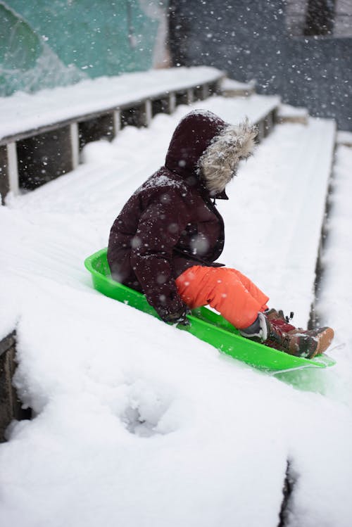 A Kid Riding the Sled on the Snow Covered Stairs
