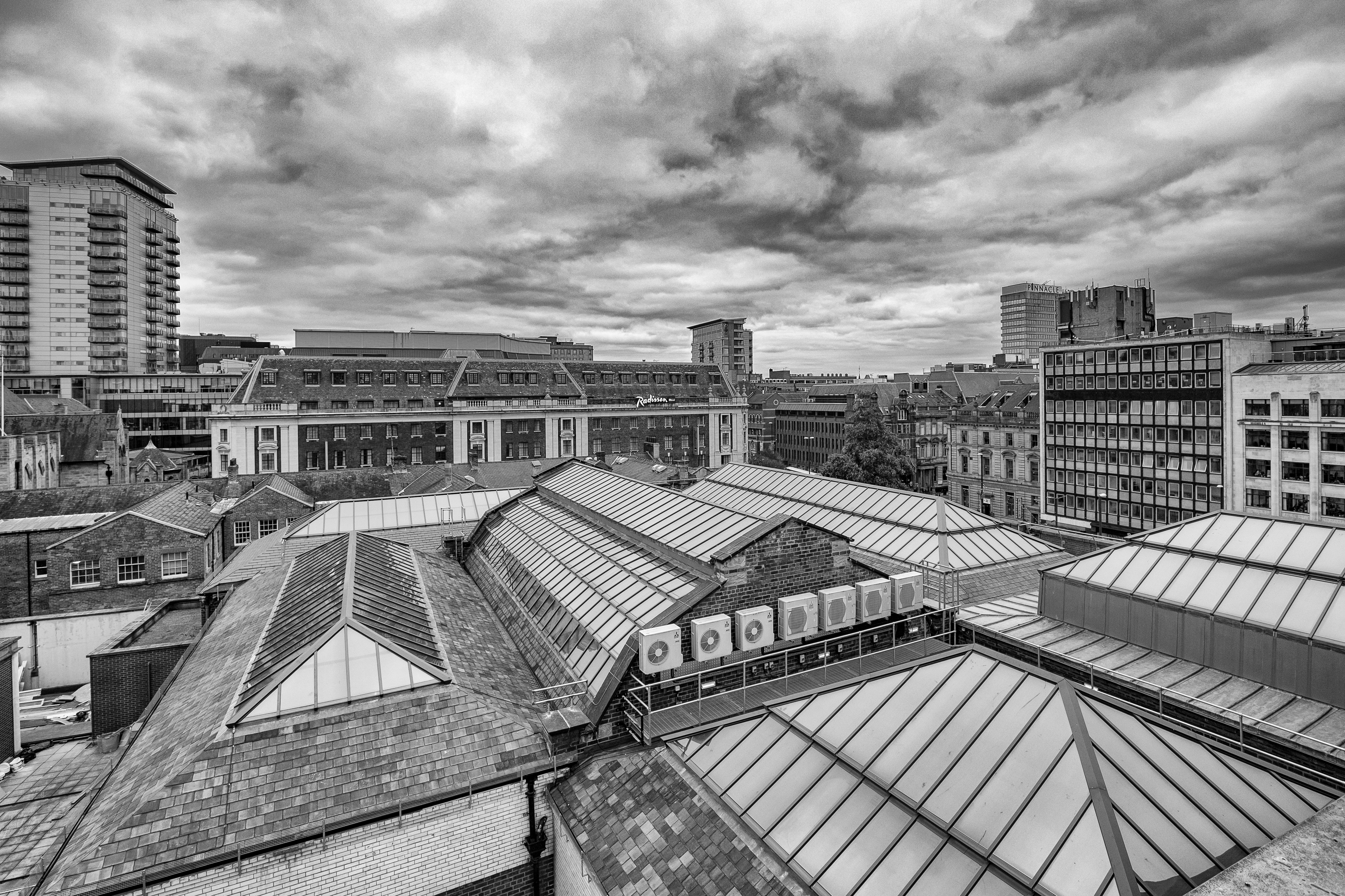 Black and white view of Leeds city rooftops amidst a cloudy sky, showcasing urban architecture.