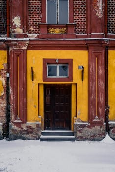 A vintage entrance with vibrant yellow walls covered in snow adds a pop of color to the winter scene.