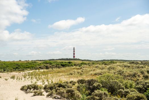 Beautiful coastal dunes with a distant red and white lighthouse under a bright sky.