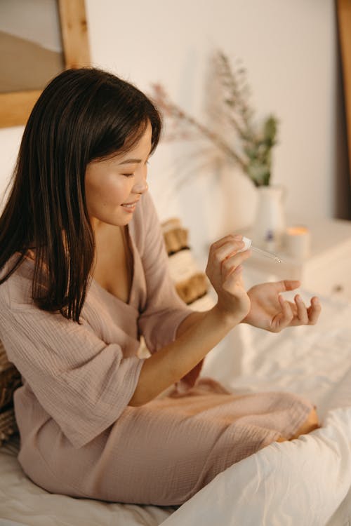 Young Woman Sitting in Bed and Applying a Cosmetic Product 