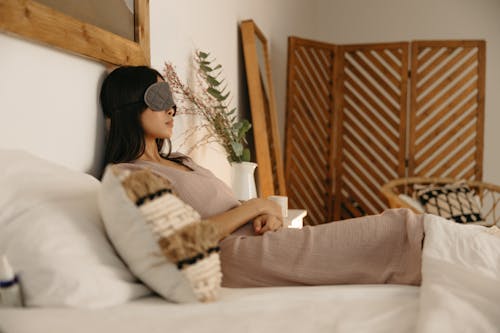 Free A Woman Sitting on Bed with a Sleep Mask Stock Photo