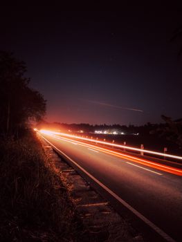 Capture of light trails on an empty highway under a starry night sky, showcasing dynamic motion and nighttime beauty.