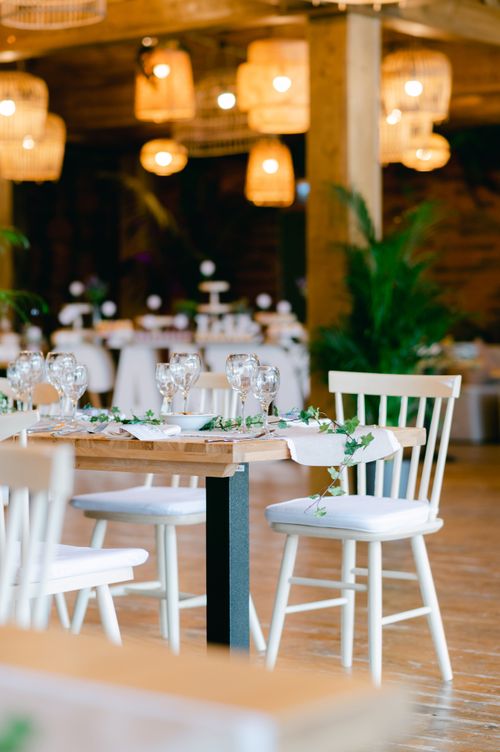Free Charming rustic wedding venue setup with wooden tables, white chairs, and ambient lighting. Stock Photo