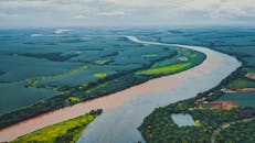 Drone view of long river streaming through lush green fields