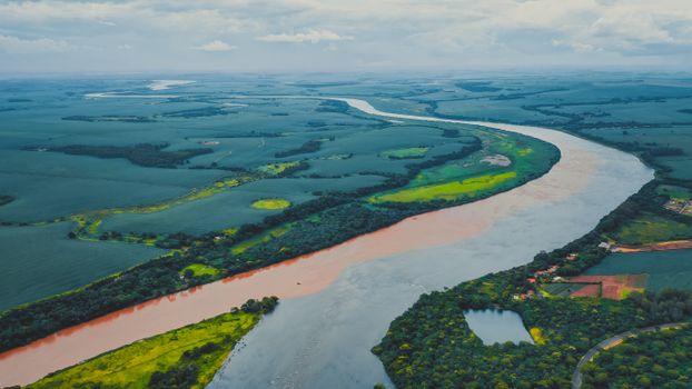 Drone view of long river streaming through lush green fields