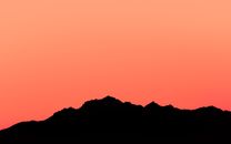Stunning silhouette of a mountain range during sunset in New Zealand with a vivid orange sky.