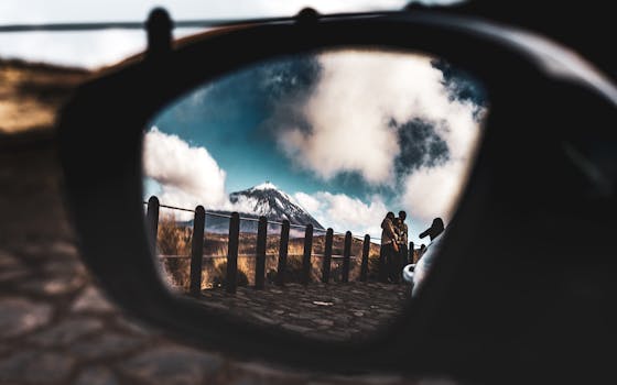 A captivating view of Mount Teide reflected in a car side mirror with people hiking nearby.