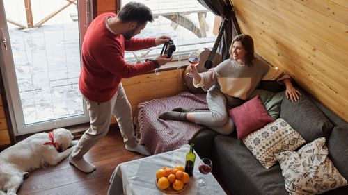Free Couple relaxing indoors with wine, guitar, and dog in a cozy winter setting. Stock Photo