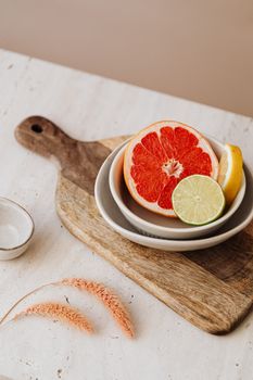 A still life composition of grapefruit, lemon, and lime slices on ceramic bowls, set on a wooden board.