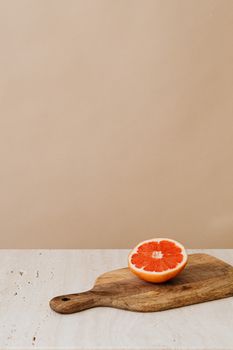 A halved grapefruit on a wooden cutting board with beige background, showcasing freshness.
