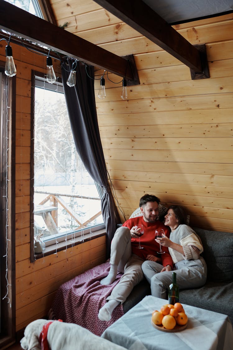 Couple Hugging On A Couch In A Cabin In Winter And Drinking Red Wine 