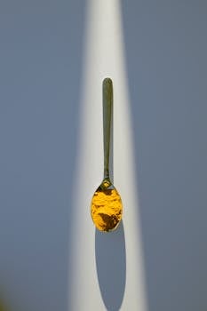 Top view of small metal spoon with yellow seasoning placed in ray of light on white table