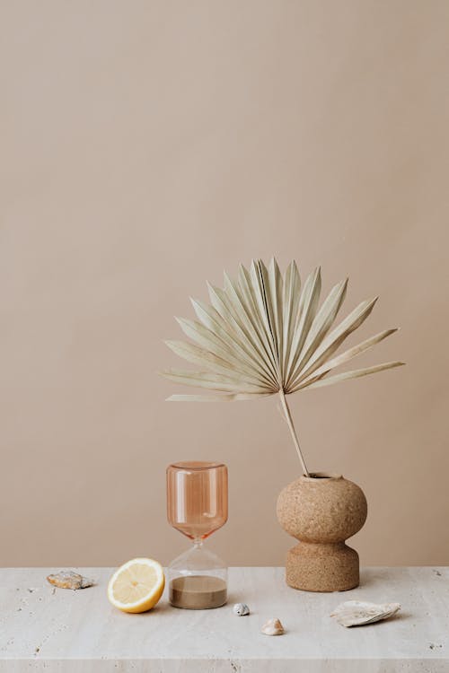 Ceramic Vase With Dried Palm Leaf Beside An Hourglass