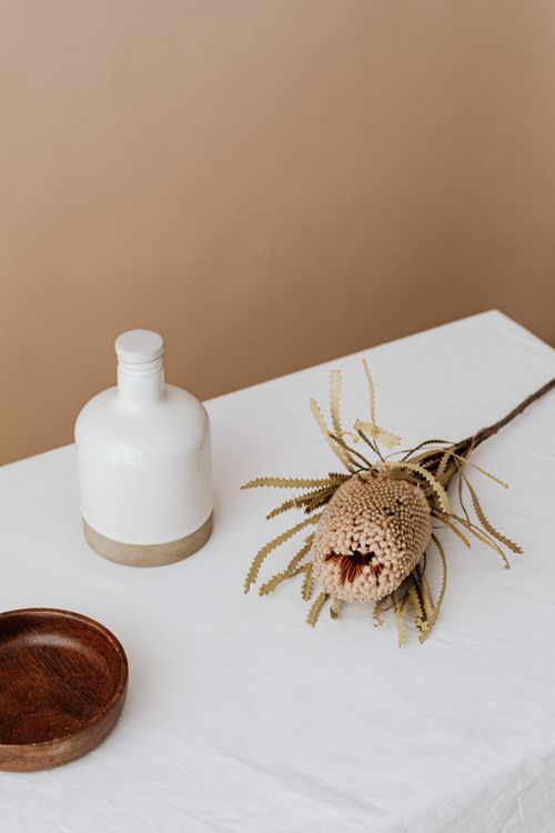 Free A minimalist still life featuring a neutral-toned flower and a white bottle on a table. Stock Photo