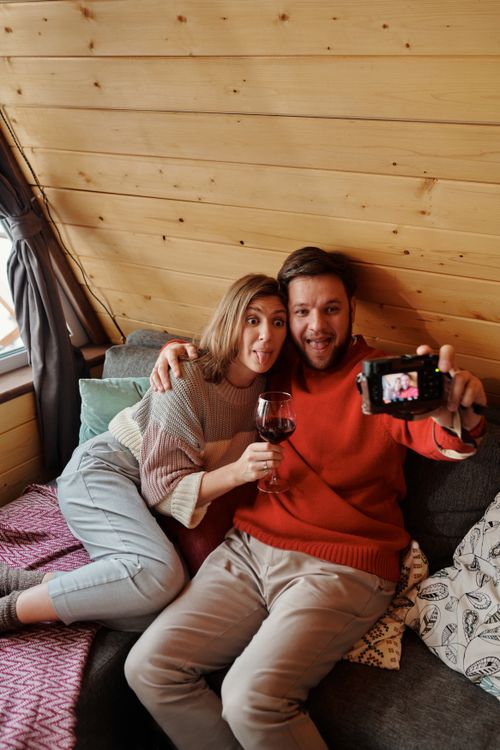 Free A cheerful couple shares a funny moment while taking a selfie indoors with wine. Stock Photo