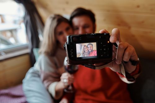 Free A couple enjoying a cozy moment indoors, capturing a selfie with a digital camera. Stock Photo