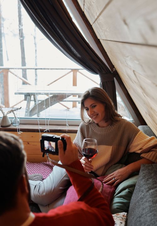 Free A woman indoors smiling and posing with a glass of wine as a photo is taken. Warm and cozy atmosphere. Stock Photo