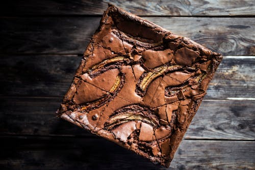 From above of tasty chocolate brownie cake with dried bananas placed on wooden table in daytime