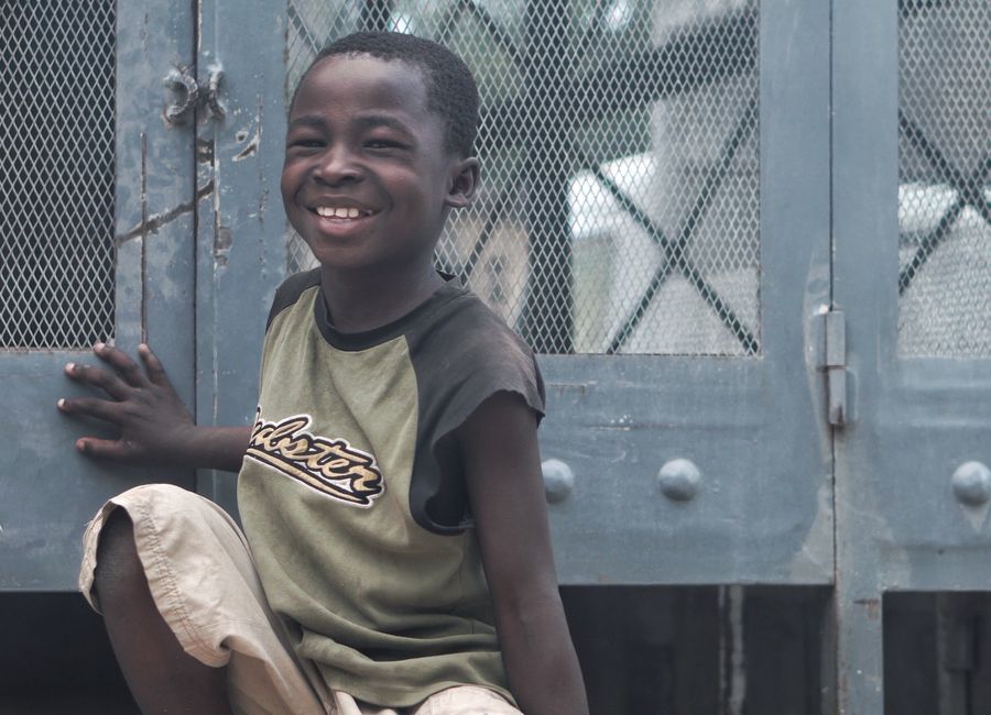 Happy child in Haiti smiles brightly while sitting outdoors.