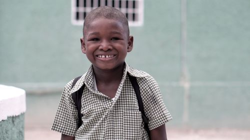 Free A cheerful Haitian boy smiling in his school uniform, showcasing innocence and happiness outdoors. Stock Photo