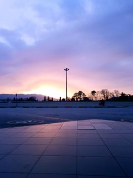 Stunning sunset view over cityscape with purple skies and silhouetted trees on horizon.