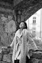 Woman In White Coat With Scarf Leaning On Rock Wall