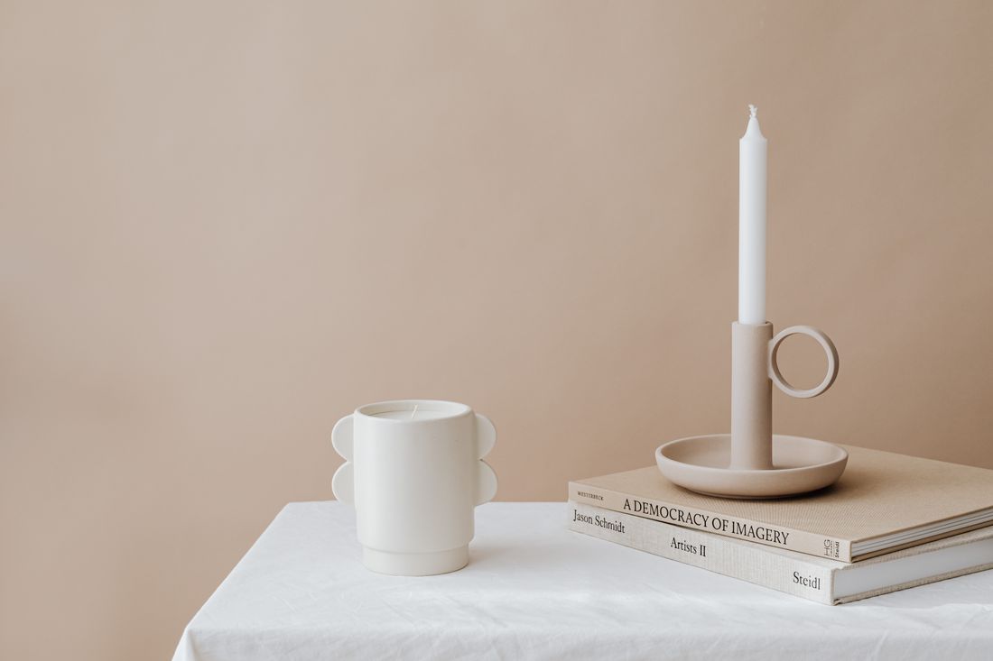 A candleholder, mug and books arranged on a beige surface