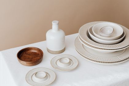 Stacked cream stoneware plates beside a matte vase, photo by Kaboompics on Pexels