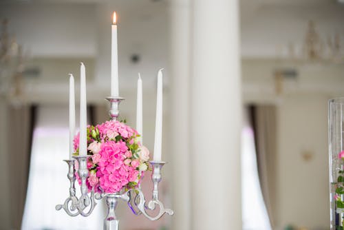 Flaming wax candle in metal candelabrum decorated with ball of flowers against blurred background of light room