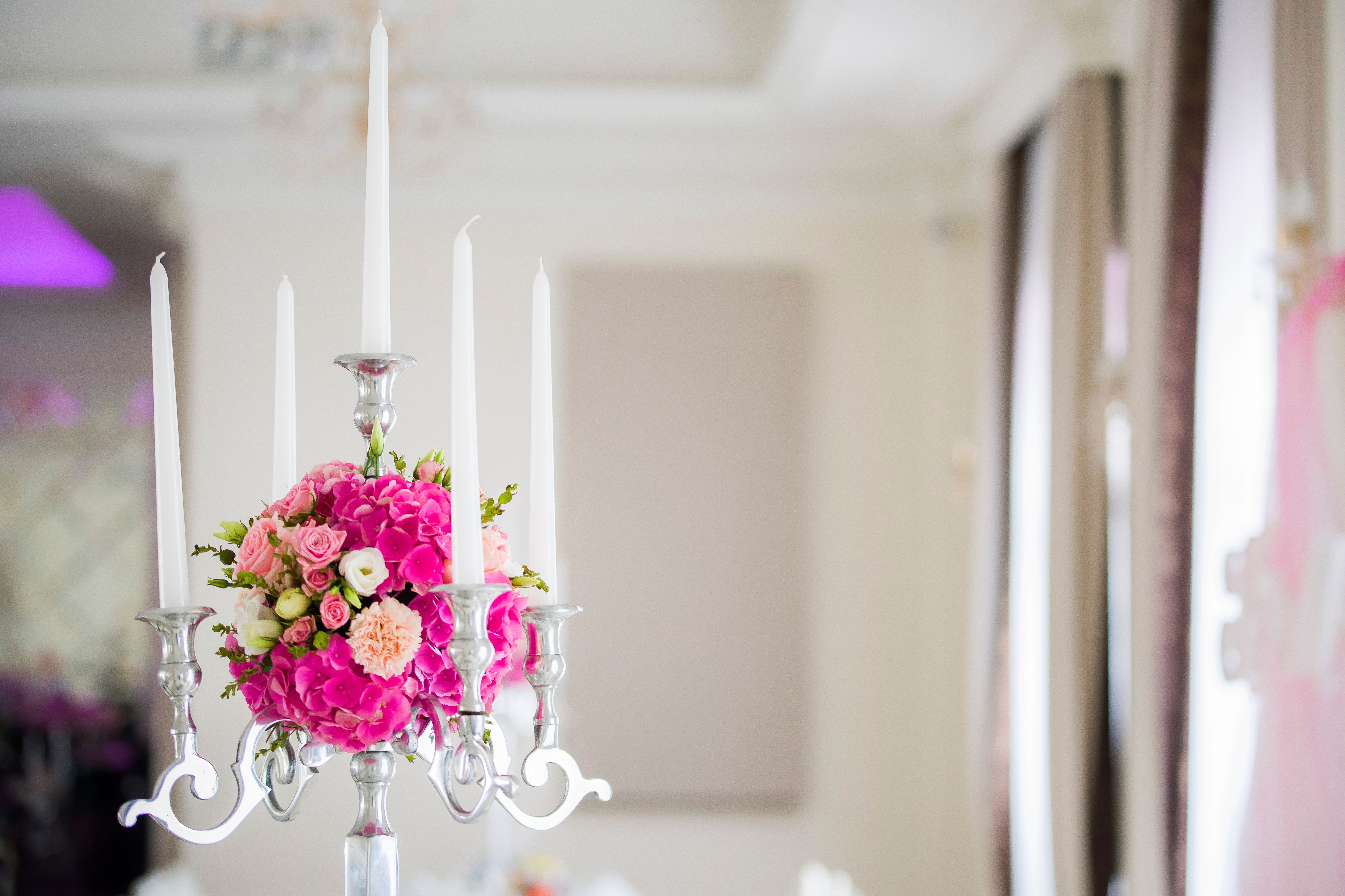 Elegant banquet table with white wax candles in metal candelabrum decorated with ball of fresh flowers in light room