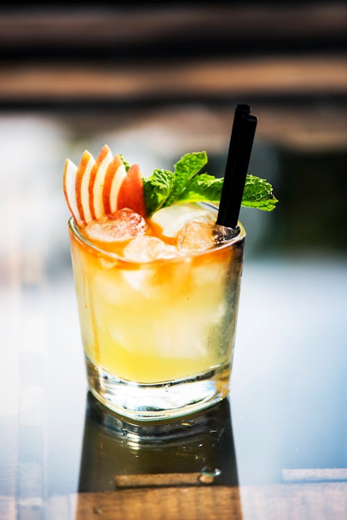 Glass of cold citrus cocktail with fresh mint and pieces of apple placed on table in daytime