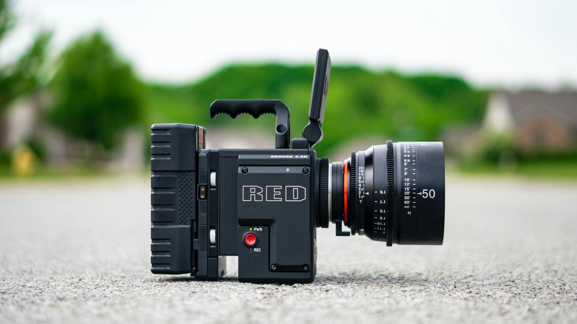 Side view of a professional RED digital cinema camera placed outdoors on a road.