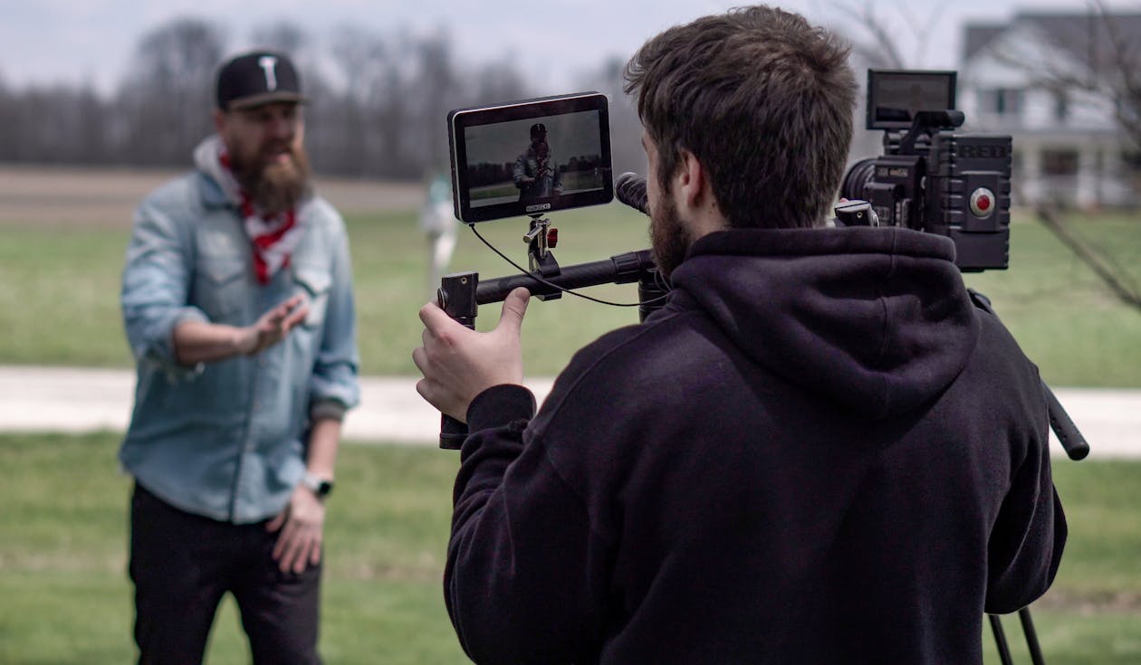 Man Filming another Man on Meadow with a Professional Camera 