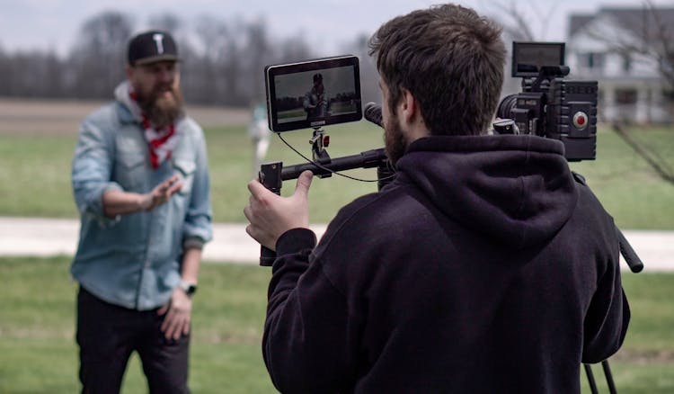 Man Filming Another Man On Meadow With A Professional Camera 