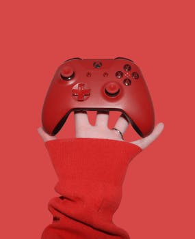 Close-up of a red Xbox controller held by a hand in red sleeve against a red background.