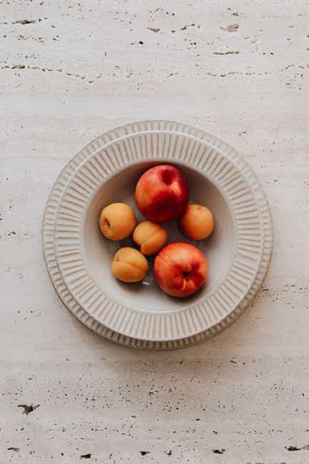 Overhead view of apricots and peaches in a rustic ceramic bowl on a textured surface.