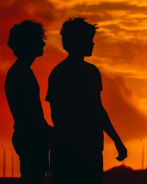 Free Two friends in silhouette captured during a vibrant orange sunset, symbolizing companionship and tranquility. Stock Photo