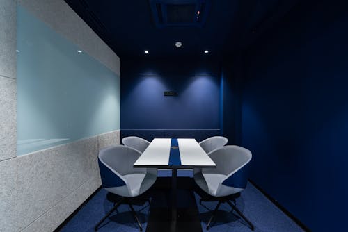 Free Comfortable chairs placed on carpet at long white desk in modern conference room with blue walls in contemporary business center Stock Photo