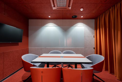 Comfortable red chairs placed around white table in modern conference room with TV and curtains in contemporary office of business center