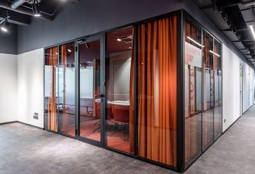 Hall of spacious contemporary business center with glass walls of modern office with colorful armchairs at table and red curtain