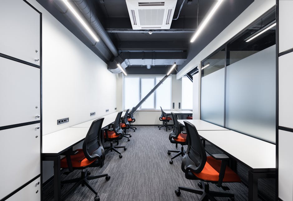 White desks with comfortable colorful chairs placed in spacious workspace with window and glass partitions in contemporary financial business center