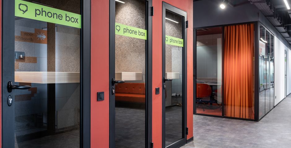 Glass phone booths beside a meeting room in a shared workspace — enclosed pods are rarely cleaned inside