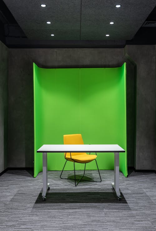 Comfortable yellow chair at white table placed on floor in modern spacious professional studio with green wall and special supply